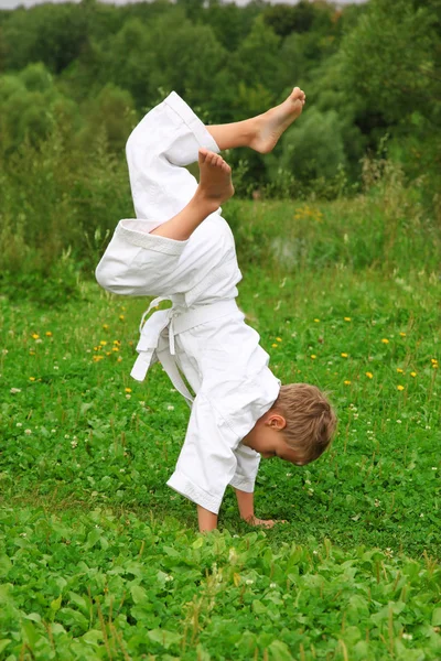 Karate chlapec dělá stojka na trávníku — Stock fotografie