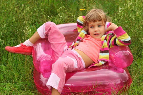 Little girl sits talks by toy phone in inflatable armchair on l — Stock Photo, Image