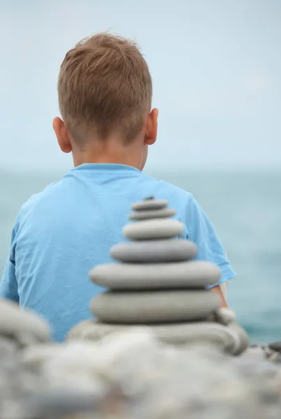 Boy and stone stack, rear view — Stock Photo, Image