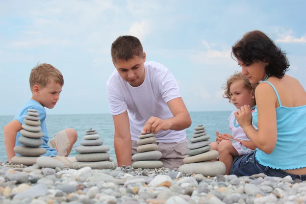 Family builds stone stacks on pebble beach — Stock Photo, Image