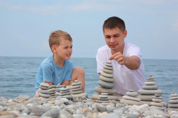 Отец и сын строят каменные стопки на галечном пляже. — стоковое фото