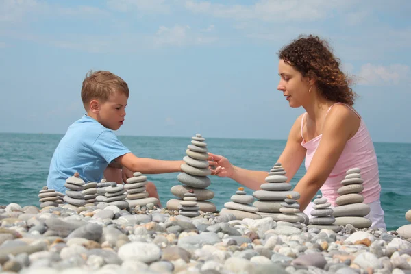 Madre e hijo construye pilas de piedra en la playa de guijarros — Foto de Stock