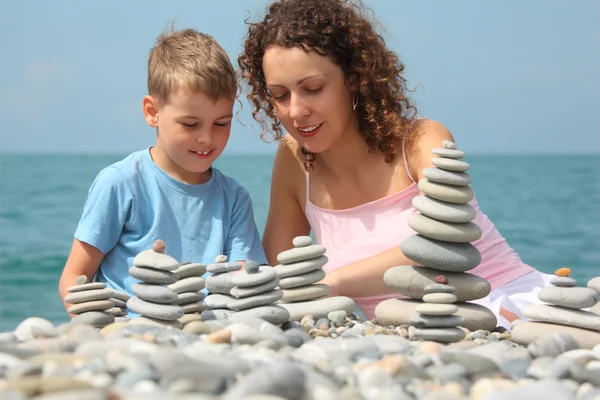 Mother and son builds stone stacks on pebble beach — Stock Photo, Image