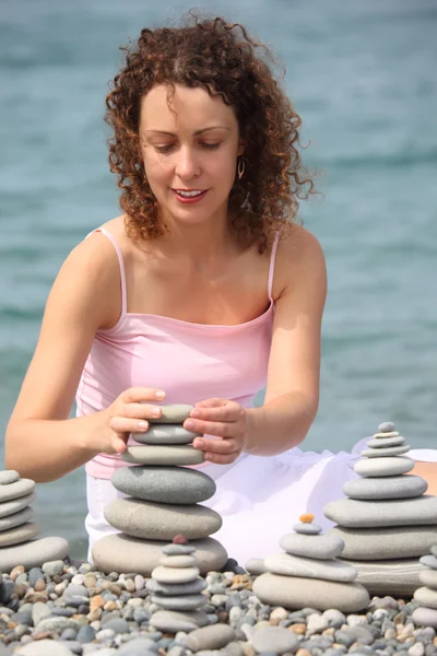 Mujer joven construye pilas de piedra en la playa de guijarros — Foto de Stock