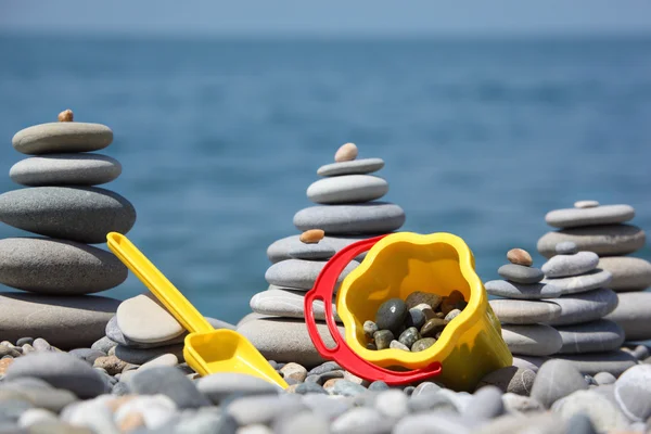 Yellow children's bucket with scoop and stone stacks on seacoas — Stock Photo, Image
