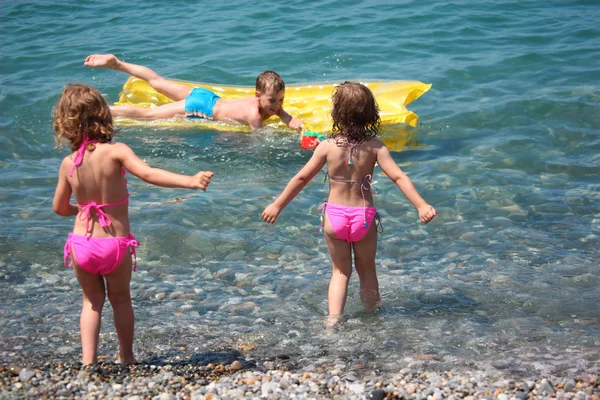Αγόρι στο φουσκωτό στρώμα στη θάλασσα και δύο κορίτσια γύρω από το ξενοδοχείο — Φωτογραφία Αρχείου