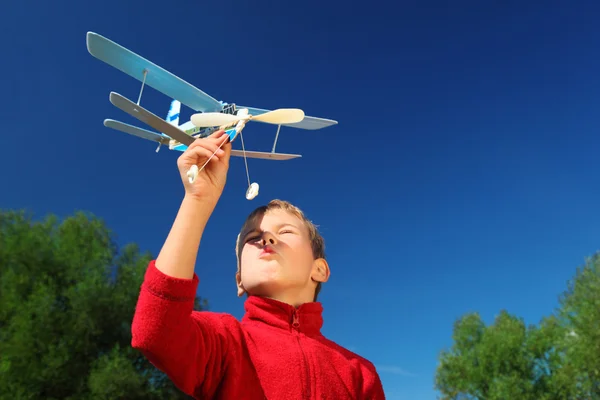 Мальчик с игрушечным самолетом в руках на открытом воздухе против неба — стоковое фото