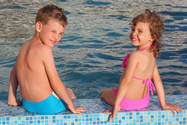 Chłopiec i dziewczynka siedzieć na skraju basenu — Zdjęcie stockowe