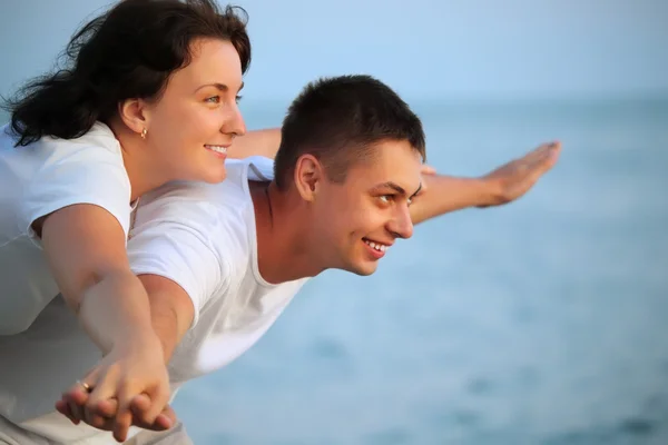 Glimlachende man en jonge vrouw handen in zijden tegen zee geplaatst — Stockfoto