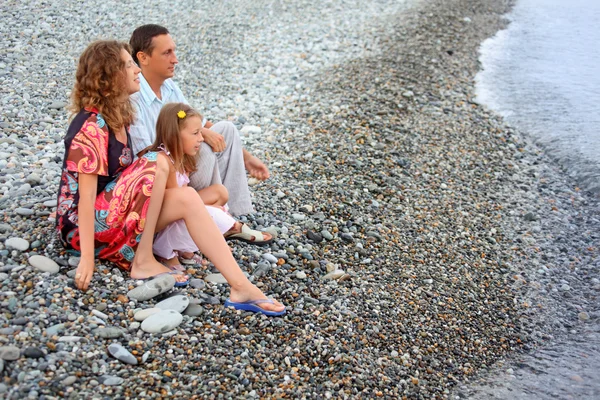 Happy family with little girl sitting on stony beach, Looking af — Stock Photo, Image