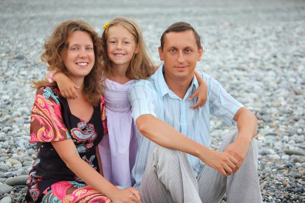 Happy family with little girl sitting on stony beach — Stock Photo, Image