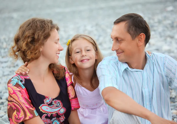 Familia feliz con niña sentada en la playa pedregosa, padres lo — Foto de Stock