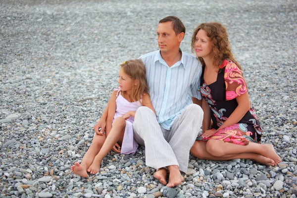 Famille heureuse avec petite fille assise sur une plage pierreuse — Photo