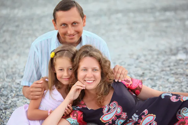 Taşlı sahilde oturan küçük kız ile mutlu bir aile — Stok fotoğraf
