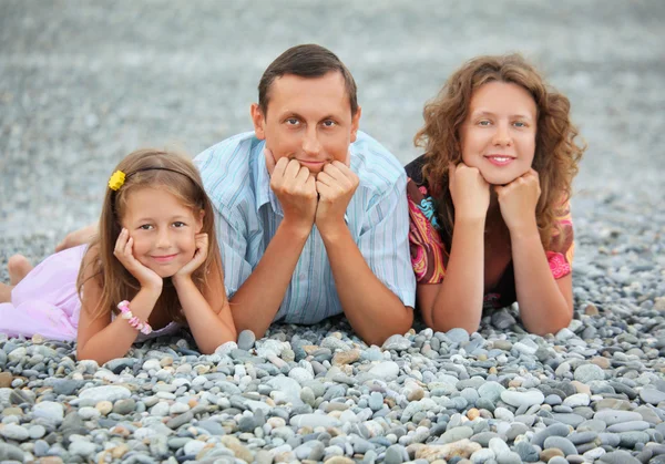 Happy family with little girl lying on stony beach, focus on fat — Stock Photo, Image