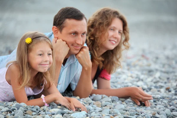 Happy family with little girl lying on stony beach — Stock Photo, Image