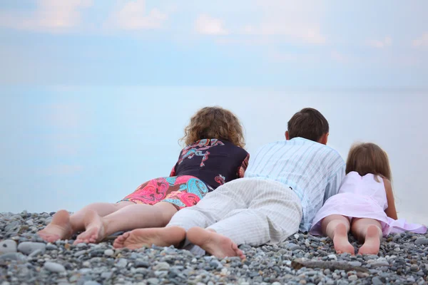 Счастливая семья с маленькой девочкой, лежащей на каменистом пляже, лежащей спиной — стоковое фото