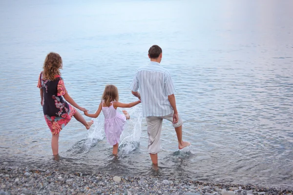 Счастливая семья с маленькой девочкой идут в воду, стоя спиной — стоковое фото
