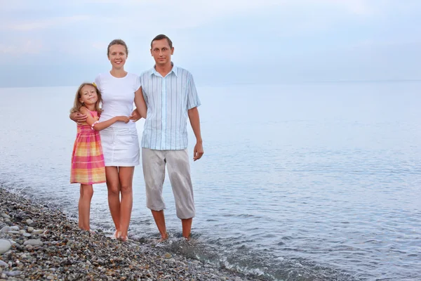 Gelukkige familie met meisje permanent op strand in avond — Stockfoto