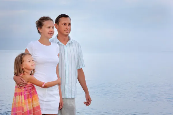 Happy family with little girl standing on beach in evening — Stock Photo, Image