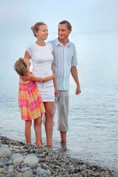 Ευτυχισμένη οικογένεια με μικρό κορίτσι στέκεται στην παραλία το βράδυ, κοιτάξτε — Φωτογραφία Αρχείου