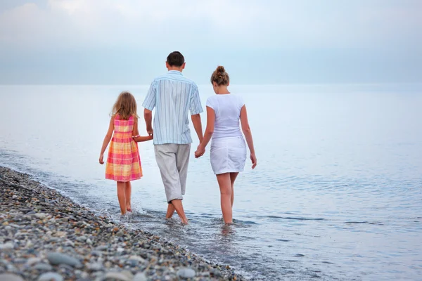 Happy family with little girl walk on beach in evening — Stock Photo, Image