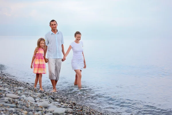 Lycklig familj med liten flicka gå på stranden på kvällen, fokus på — Stockfoto