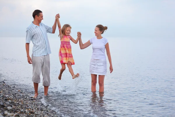 Happy family with little girl on beach in evening, parents lift — Stock Photo, Image