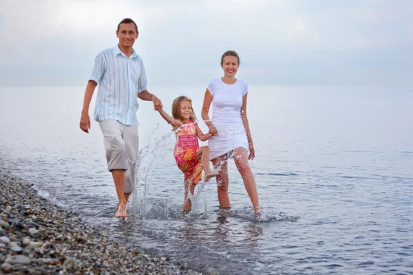 Happy family with little girl splashes feet water on beach in ev — Stock Photo, Image