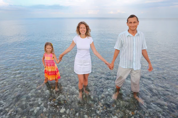 Familia feliz con la niña de pie hasta las rodillas en el mar en la playa —  Fotos de Stock