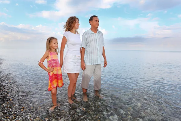 Lycklig familj med liten flicka stående knäna i havet på stranden — Stockfoto