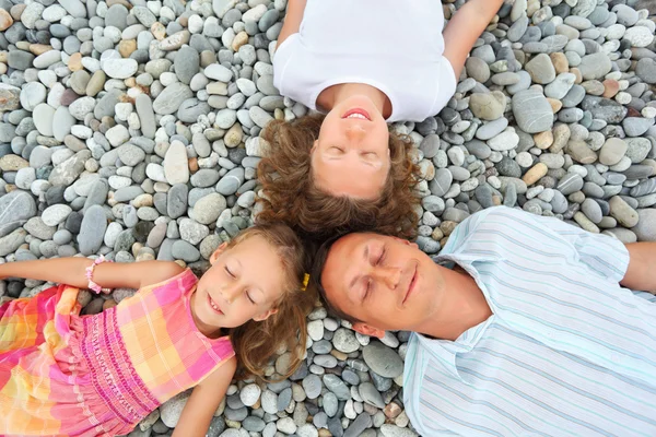 Happy family with little girl lying on stony beach, closed eyes, — Stock Photo, Image