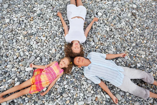 Happy family with little girl lying on stony beach, closed eyes, — Stock Photo, Image