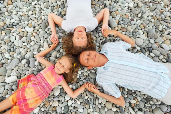 Família feliz com a menina deitada na praia de pedra, olhos fechados , — Fotografia de Stock