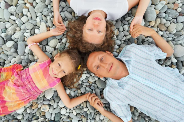 Familia feliz con la niña mintiendo en la playa pedregosa, teniendo unirse — Foto de Stock