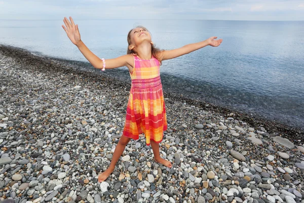 Little girl lifted hands upwards on stony beach — Stock Photo, Image