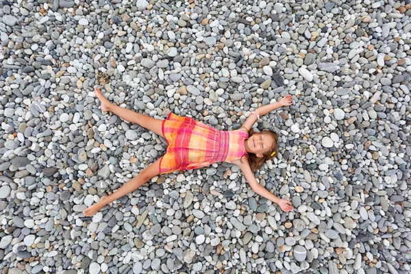 Little girl lying on stones on stone seacoast — Stock Photo, Image
