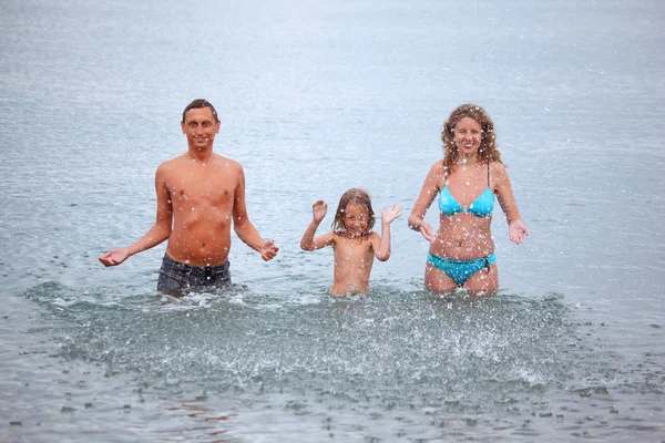 Família feliz com a menina espirra mãos de água de pé em b — Fotografia de Stock
