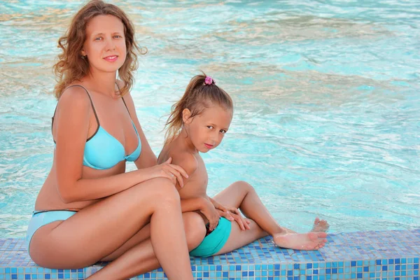 Güzel bir kadın ve küçük bir kız havuza yakın otururlar. — Stok fotoğraf