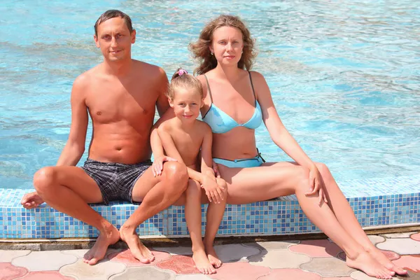 Familia feliz con niña sentada cerca de la piscina — Foto de Stock