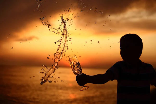 Σιλουέτα του αγόρι θα χυθεί έξω από το ποτό από το γυαλί για θάλασσα ηλιοβασίλεμα — Φωτογραφία Αρχείου