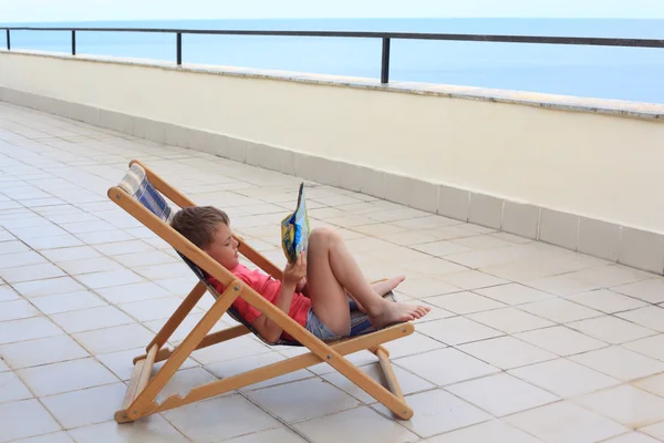 Kleiner Junge liest in Lounge auf Veranda — Stockfoto