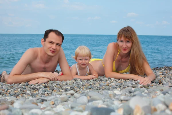 Parents with child on sea coast lie on pebble — Stock Photo, Image