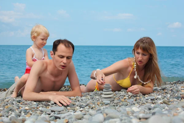 Parents with child on sea coast build pyramid of stones — Stock Photo, Image