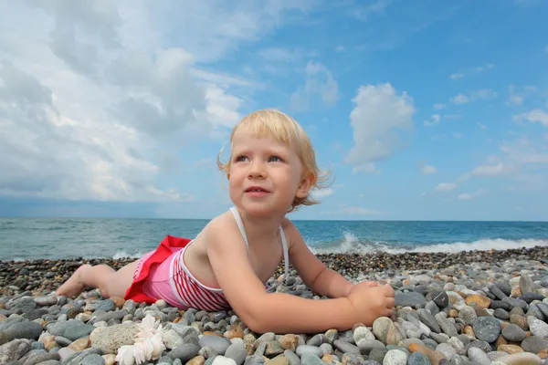 Child lies on pebble beach — Stock Photo, Image