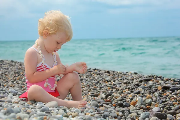 Child sits on pebble beach — Stock Photo, Image