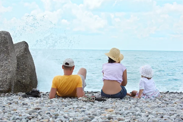 Parents with child sit on seacoast, rear view — Stock Photo, Image
