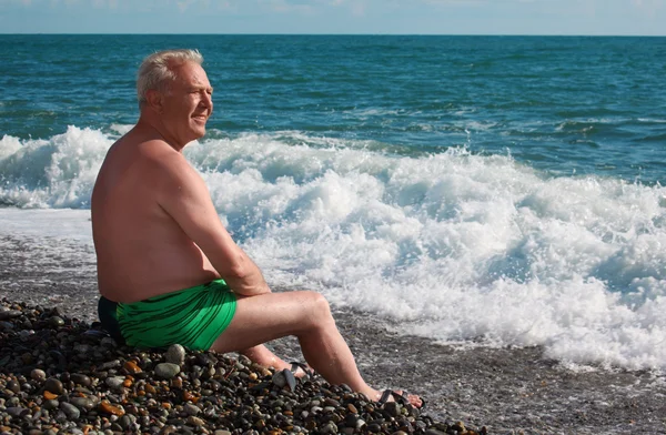 Пожилой человек сидит на берегу моря — стоковое фото