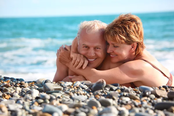 Happy aged pair lie on pebble beach — Stockfoto