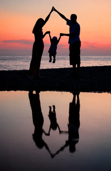 Silhouettes of parents with child against sea decline — Stockfoto